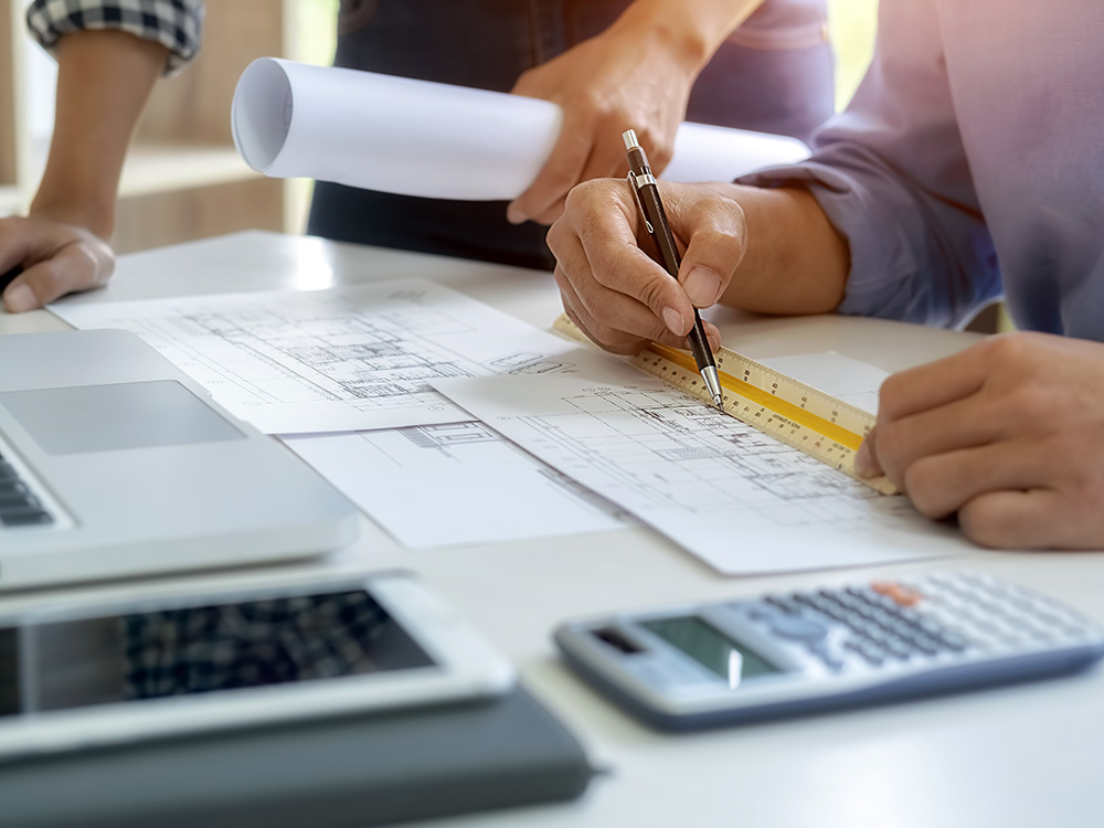 Gutachten & Wertermittlung – Immobilien sachverständig prüfen Hände mit Stift und Lineal über Bauplänen am Schreibtisch mit Laptop und Taschenrechner